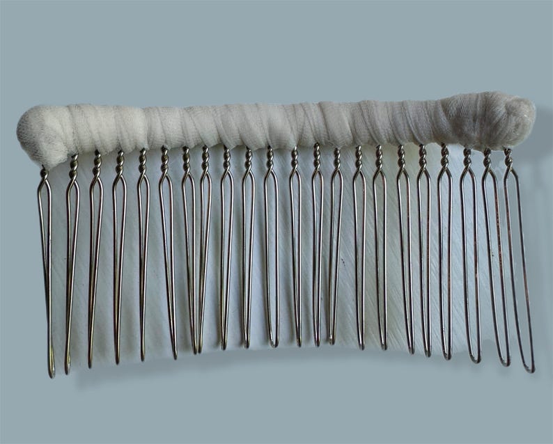 May include: A vintage hair comb with a white, fabric-wrapped top and silver-toned metal teeth. The teeth are evenly spaced and have a looped design at the top. The comb is designed for securing hair in place.