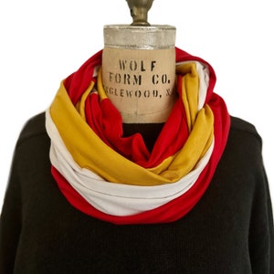 K&ouml;nnte beinhalten: Ein mehrfarbiger Loop-Schal in Rot, Gelb und Wei&szlig; ist um den Hals einer Schaufensterpuppe drapiert. Der Schal ist aus weichem Stoff gefertigt und wird vor einem schwarzen Pullover pr&auml;sentiert. Auf der Schaufensterpuppe steht "WOLF FORM CO. ENGLEWOOD, N".