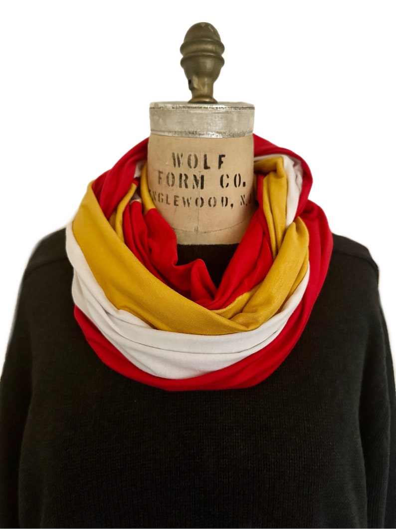 K&ouml;nnte beinhalten: Ein mehrfarbiger Loop-Schal in Rot, Gelb und Wei&szlig; ist um den Hals einer Schaufensterpuppe drapiert. Der Schal ist aus weichem Stoff gefertigt und wird vor einem schwarzen Pullover pr&auml;sentiert. Auf der Schaufensterpuppe steht "WOLF FORM CO. ENGLEWOOD, N".