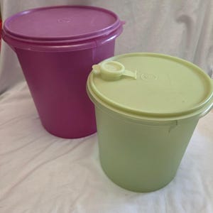 May include: Two cylindrical plastic storage containers with lids. One container is deep magenta with a solid matching lid. The other container is light lime green and features a lid with a small, circular, hinged flip-top spout opening.