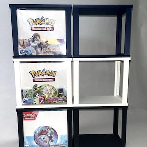 Könnte beinhalten: Ein vertikales Aufbewahrungsregal mit sechs quadratischen Fächern und dunkelblauen sowie weißen Rahmen. Drei Fächer enthalten versiegelte Pokémon Trading Card Game Booster-Boxen, darunter die Editionen Paldea Evolved und Scarlet & Violet.