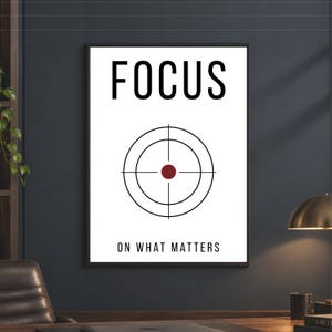 Pode incluir: Uma impressão de arte de parede retangular com fundo branco e a palavra FOCUS em letras maiúsculas pretas no topo. Abaixo, um gráfico circular preto de um alvo com um ponto central vermelho escuro. O texto ON WHAT MATTERS é preto.