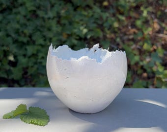 Small light-gray concrete vessel sculpture. Sustainable. Live edge. Bowl has an outside surface partly shiny & partly matte. Wabi-sabi.