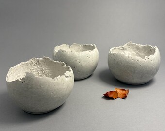 Three small light-gray concrete vessel sculptures. Sustainable. Live edge. Bowls have a natural shiny outside surface. Wabi-sabi style.