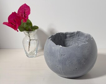 Small medium-gray concrete vessel sculpture. Sustainable. Live edge. Partly shiny outside surface, textured interior. Wabi-sabi style bowl.