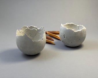 Two small light-gray concrete vessel sculptures. Sustainable. Live edge. Bowls with a natural shiny outside surface. Wabi-sabi style.