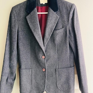 May include: A charcoal gray wool-blend blazer featuring a dark navy blue velvet collar, a deep burgundy interior lining, two front patch pockets, a single chest pocket, and two brown buttons centered on the front closure.