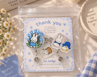 Puede incluir: Dos portatarjetas de acrílico con personajes de dibujos animados, uno con un conejo blanco entre flores azules y el otro con un conejo blanco y un pingüino azul, en una tarjeta a cuadros azul claro con el texto thank you for supporting my small business.
