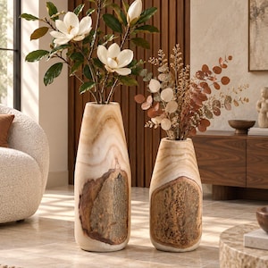 Peut inclure: Deux grands vases cylindriques en bois avec une finition lisse et claire et une incrustation d'écorce texturée sur le devant. Le vase le plus haut contient des fleurs de magnolia blanches avec des feuilles vertes, et le plus petit des feuillages séchés.