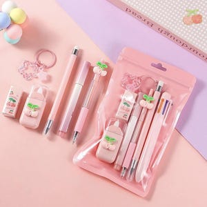 Peut inclure: Un ensemble de papeterie composé d'articles roses et blancs, notamment des stylos, un porte-mine, un ruban correcteur et une gomme, tous ornés de petits motifs de cerises. Un porte-clés rose assorti et une pochette transparente sont inclus.