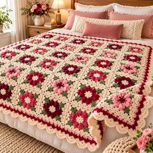 Pode incluir: Uma manta de crochê feita à mão com um padrão quadrado repetitivo de motivos florais em tons de creme, rosa claro, rosa escuro e vermelho profundo, acentuado com folhas verde-escuras e um acabamento de borda festonada creme.