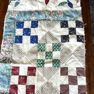 May include: A rectangular patchwork quilt runner featuring a top border with appliqued fabric leaves on a cream background. The body consists of alternating blocks of floral, checkered, and solid-colored fabric squares in blue, red, green, and brown.