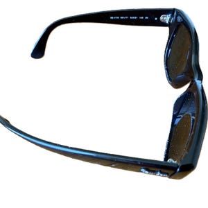 Puede incluir: Gafas de sol negras con lentes oscuras. Las gafas tienen un dise&ntilde;o cl&aacute;sico con montura gruesa y patillas curvas. El texto "RB 4178 601/71 52021 140 3N" est&aacute; impreso en el interior de la patilla izquierda.