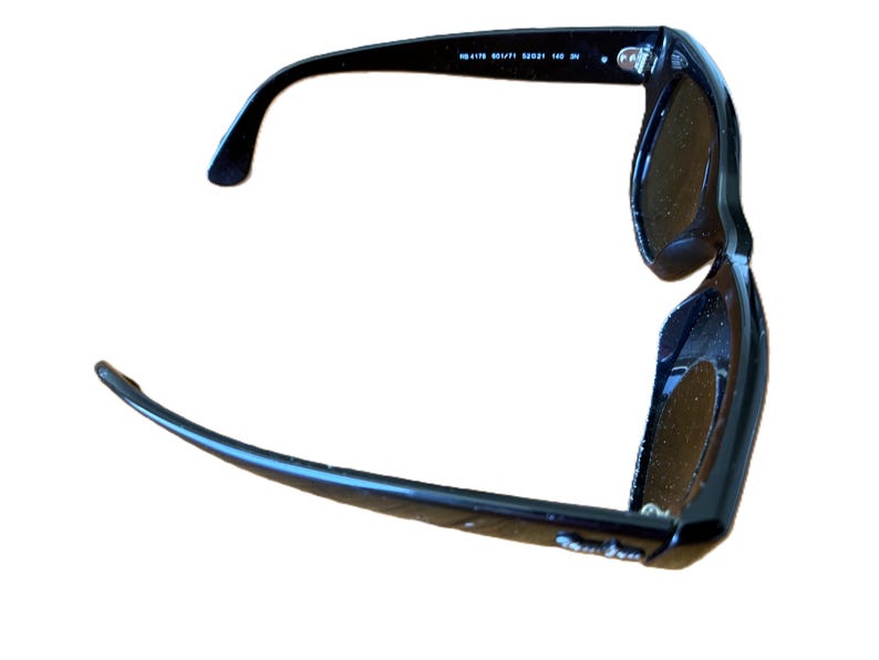 Puede incluir: Gafas de sol negras con lentes oscuras. Las gafas tienen un dise&ntilde;o cl&aacute;sico con montura gruesa y patillas curvas. El texto "RB 4178 601/71 52021 140 3N" est&aacute; impreso en el interior de la patilla izquierda.