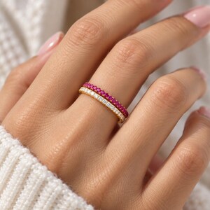 May include: A stack of two thin gold rings featuring a pav&eacute; setting. The top ring is adorned with a continuous row of vibrant pink stones, while the bottom ring features a matching row of clear, sparkling white stones set in a gold band.