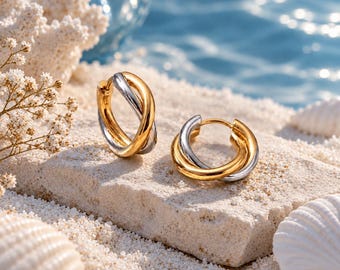 May include: A pair of hoop earrings featuring an intertwined design with alternating polished gold and silver-toned metal bands. The earrings have a circular shape with a hinged closure mechanism, showcasing a two-tone metallic finish.