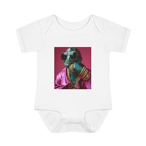May include: A white short-sleeved baby bodysuit featuring a central graphic print of a green turtle wearing black sunglasses, a pink collared shirt, a gold chain necklace, and multiple gold bracelets on its wrist against a dark pink background.