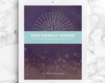 May include: A digital tablet displaying a purple and gold background with a compass graphic and the text "BRAND PERSONALITY WORKBOOK" in white. The text below reads "NAVIGATE THE PERSONALITY OF YOUR BRAND TO FIND FOCUS, CLARITY AND THE EMOTIONAL FRAMEWORK FOR YOUR VISUAL IDENTITY" in white. The text at the bottom reads "by amanda cecek creative" in white.