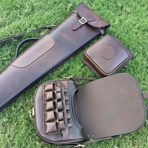 May include: A dark brown leather long case with a buckle strap, a square leather pouch with a circular embossed detail, and a leather shoulder bag featuring a front panel with multiple small vertical pockets and a large open flap closure.