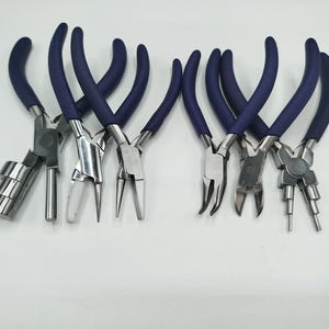 May include: A set of six metal jewelry pliers featuring dark blue rubberized handles. The collection includes specialized tools such as bail-making pliers with stepped cylindrical jaws, needle-nose pliers, bent-nose pliers, and wire cutters.