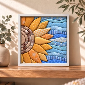 May include: A square framed wall art piece featuring a layered fabric sunflower design. The sunflower petals are made of various yellow and orange patterned textiles, while the centre consists of brown and beige checkered fabric squares.