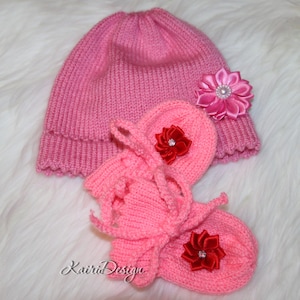 May include: Pink knitted baby hat and booties with pink and red flower embellishments.