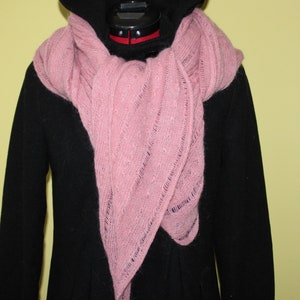 May include: A pink knitted scarf draped over a black hooded coat. The scarf is a triangular shape with a delicate openwork pattern.