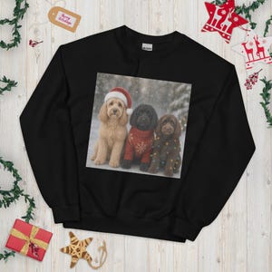 May include: A black crewneck sweatshirt featuring a graphic print of three dogs in a snowy setting. One dog wears a red Santa hat, another wears a red jumper with a white snowflake pattern, and the third is wrapped in colourful string lights.