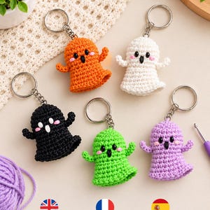 May include: Five crocheted ghost keychains in orange, white, black, green, and purple. Each ghost features two black bead eyes, a small black mouth, and two pink stitched cheeks. Each figure is attached to a silver-toned metal keyring.