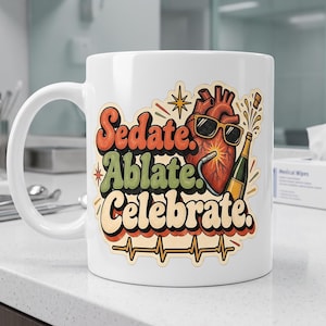 May include: A white ceramic mug featuring a colorful graphic with the text Sedate. Ablate. Celebrate. The design includes a stylized anatomical heart wearing sunglasses, holding a champagne bottle, and a heartbeat line at the bottom.
