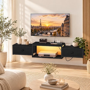 May include: A black wall-mounted floating media console featuring two side drawers with round knobs and a central open shelf illuminated by warm internal lighting. The unit is positioned directly beneath a flat-screen television.