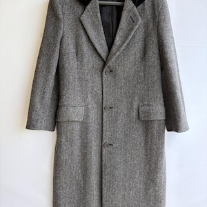 May include: A long, grey herringbone coat featuring a contrasting black velvet collar, long sleeves, and a three-button front closure. The coat includes two side flap pockets and is fully lined in black fabric, hanging on a black plastic hanger.