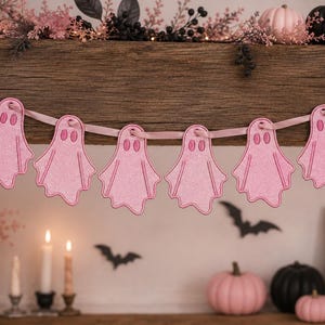 May include: A decorative garland featuring six glittery pink ghost-shaped cutouts strung together on a light pink satin ribbon. Each ghost has two oval-shaped eye cutouts and is finished with a matching pink satin bow tied at each end of the ribbon.