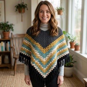 May include: A crochet poncho featuring a V-shaped pattern with horizontal stripes in charcoal gray, mustard yellow, cream, and teal. The garment has a high neckline and is finished with long, dark charcoal gray fringe along the bottom edge.