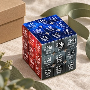 May include: A puzzle cube featuring a periodic table design with colored faces. Each square displays an element symbol, atomic number, name, and mass. The cube has blue, red, and dark gray sections with white text, showcasing elements from Hydrogen to Cobalt.