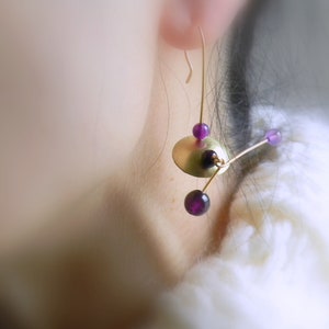 May include: Gold earrings with purple beads and a gold disc. The earrings are dangling and have a geometric design.