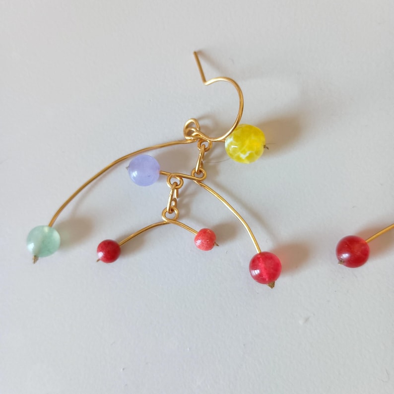 Peut inclure: Boucle d'oreille en fil d'or au design abstrait unique. La boucle d'oreille pr&eacute;sente une s&eacute;rie de perles color&eacute;es dans les tons de rouge, jaune, vert et violet. Les perles sont fix&eacute;es au fil dans un agencement artistique et &eacute;quilibr&eacute;.