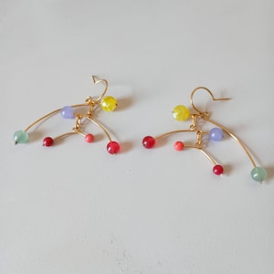 Peut inclure: Une paire de boucles d'oreilles en fil d'or avec des perles color&eacute;es. Les boucles d'oreilles pr&eacute;sentent un design incurv&eacute; avec des perles rouges, roses, jaunes, vertes et violettes. Elles ont une fermeture &agrave; crochet.