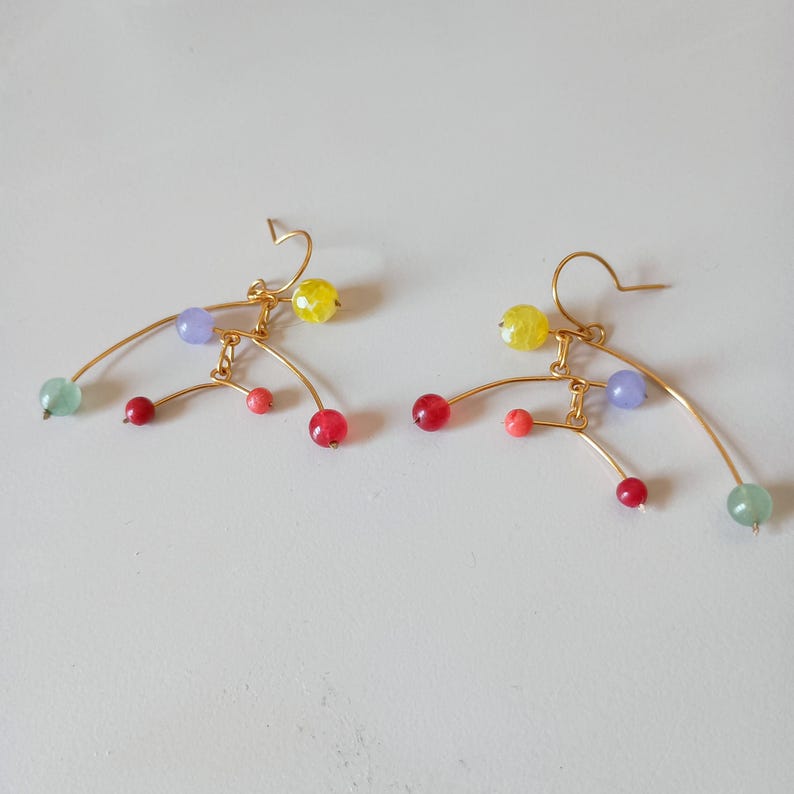 Peut inclure: Une paire de boucles d'oreilles en fil d'or avec des perles color&eacute;es. Les boucles d'oreilles pr&eacute;sentent un design incurv&eacute; avec des perles rouges, roses, jaunes, vertes et violettes. Elles ont une fermeture &agrave; crochet.