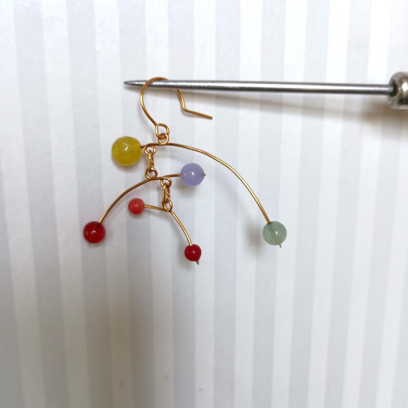 Peut inclure: Boucle d'oreille en fil dor&eacute; avec un crochet, orn&eacute;e d'une s&eacute;rie de perles color&eacute;es. Les perles sont dans les tons de rouge, jaune, violet et vert. La boucle d'oreille a un design d&eacute;licat et abstrait.