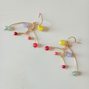 Peut inclure: Une paire de boucles d'oreilles dor&eacute;es au design abstrait unique. Chaque boucle d'oreille pr&eacute;sente un fil incurv&eacute; orn&eacute; de perles color&eacute;es rouges, jaunes, vertes et violettes. Les perles sont de tailles vari&eacute;es, ajoutant de l'int&eacute;r&ecirc;t visuel.