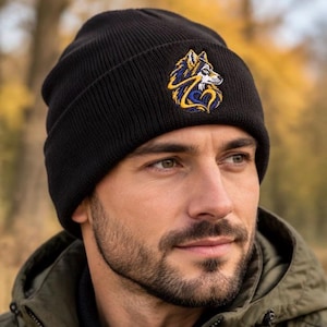 May include: A black knit beanie featuring an embroidered patch on the front. The patch displays a stylized wolf head design in shades of blue, yellow, and white, with the wolf's fur forming a heart shape around its neck area.