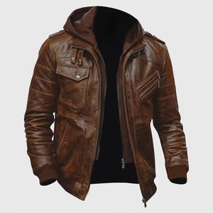 May include: A brown leather jacket featuring a dark brown integrated hood, a front zip fastening, and multiple pockets. The jacket includes shoulder epaulettes, ribbed cuffs, and a textured finish with visible stitching details across the chest and sleeves.