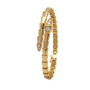 May include: A gold bracelet designed in a coiled snake shape with a segmented body. The head and tail sections are accented with small, round, clear, sparkling stones set into the metal. The bracelet features a polished finish and a clasp.