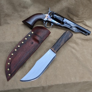 May include: A classic revolver with a dark wood handle and a blued steel finish, next to a large hunting knife with a wooden handle and a leather sheath. The knife has a silver blade and a copper bolster. The sheath is brown leather with brass rivets.
