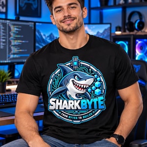 Puede incluir: Una camiseta negra de manga corta con un gráfico circular de un tiburón con un patrón de circuito, cubos azules y el texto SHARKBYTE FROM BYTES TO BUILDS en letras blancas y azules centrado en el pecho de la prenda.