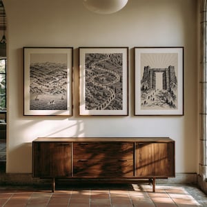 May include: Three framed vertical art prints displayed in a row, featuring detailed black and white ink-style illustrations of landscapes, a winding path through hills, and a large stone gateway with figures walking toward it under sun rays.
