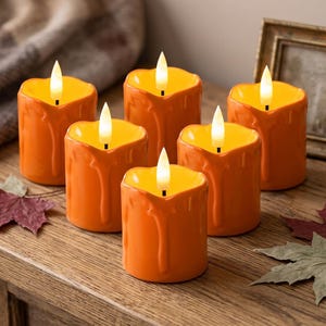 May include: A set of six orange battery-operated pillar candles with a melted wax drip design. Each candle features a warm, glowing LED flame at the top. The candles are arranged in a cluster, creating a bright, illuminated display of orange light.