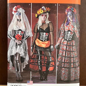 Op de afbeelding: Simplicity naaipatroon 1033 H5 voor kostuums met drie variaties van skelet-outfits met kant, bloemenhoofddeksels en hoepelrokken. De verpakking toont de maten 32-40 en bevat illustraties van de voltooide kledingstukken.