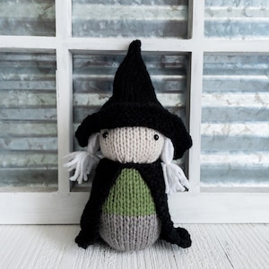 May include: A knitted witch doll with a black hat, white hair, and a green and gray dress.